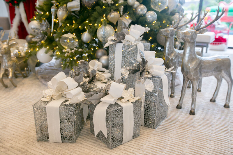 Silver-wrapped holiday presents with white ribbon bows arranged under a Christmas tree, styled with metallic reindeer figures and twinkling lights, showcasing premium holiday styling by Interiors by CV.