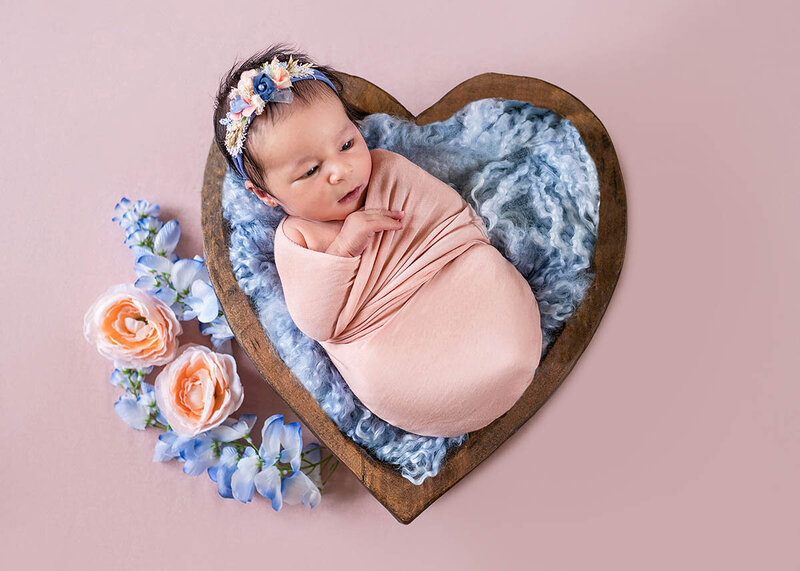 Twin baby girls sleeps in pink swaddles on a bed of pink flowers