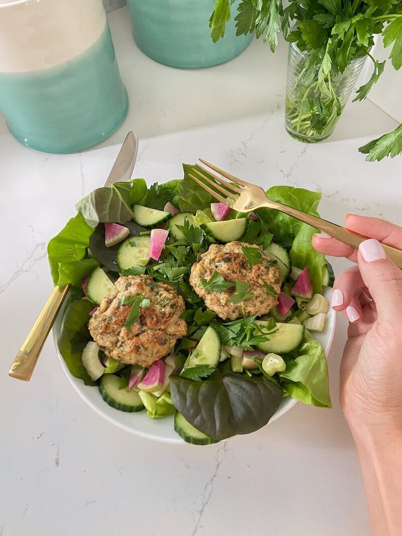 A green salad with canned salmon patties on top.