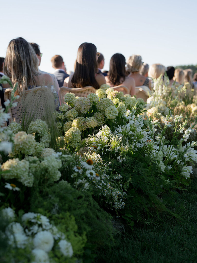 White and green wedding ceremony florals with guests seated in the background