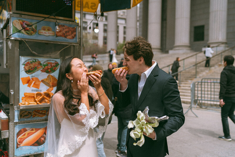 couple eating hot dogs outside in wedding attire, shot by elsie goodman photography