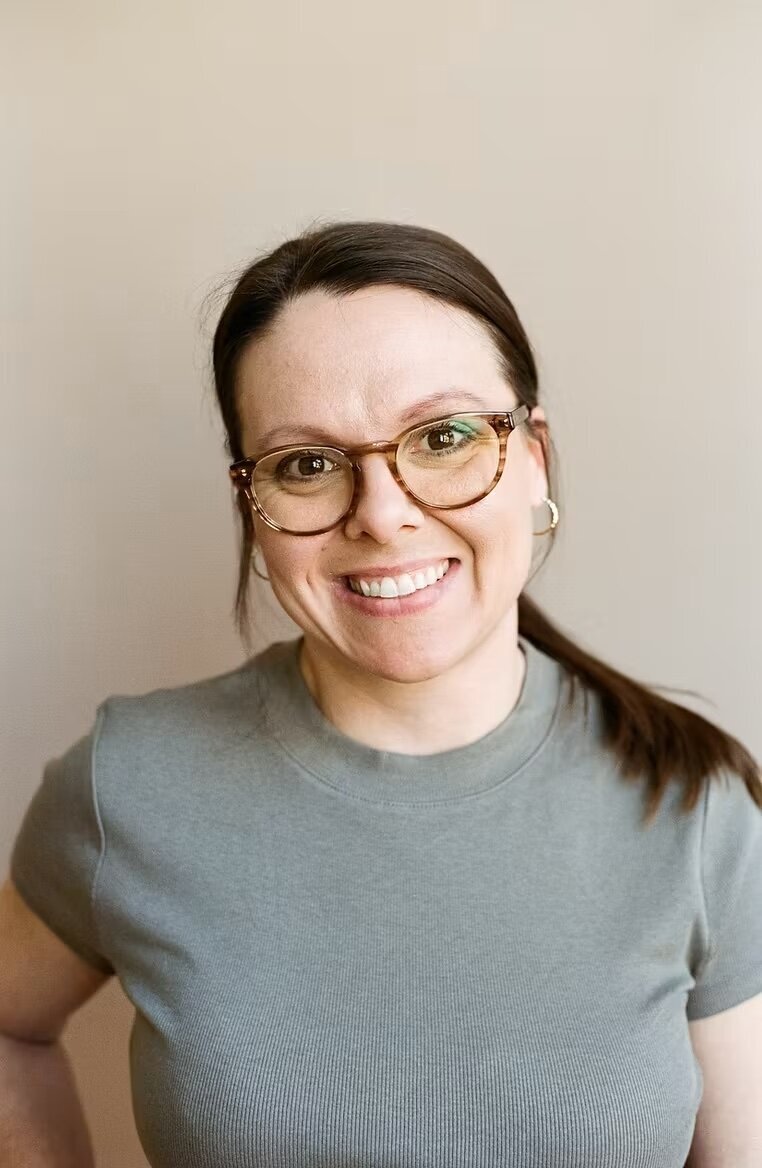 A woman wearing glasses and a gray shirt, representing a therapist in Evanston, IL, engaged in a professional setting.