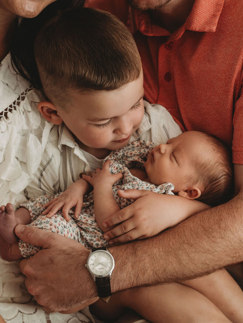 Toddler boy holding newborn baby sister during newborn photo session.