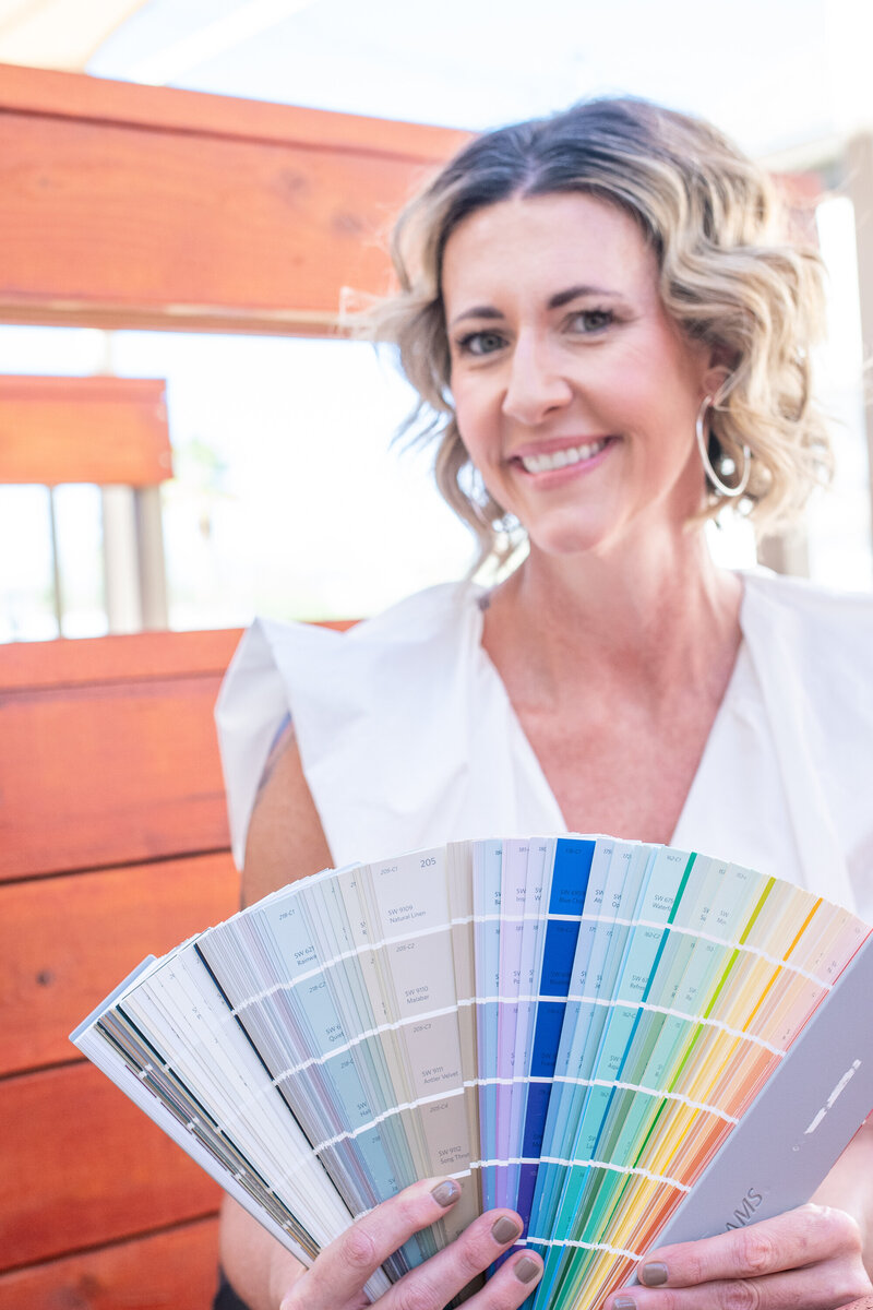 Smiling woman holding a large fan of colorful paint swatches while sitting outdoors, photographed by Vyrl Photo, showcasing Tucson brand photography