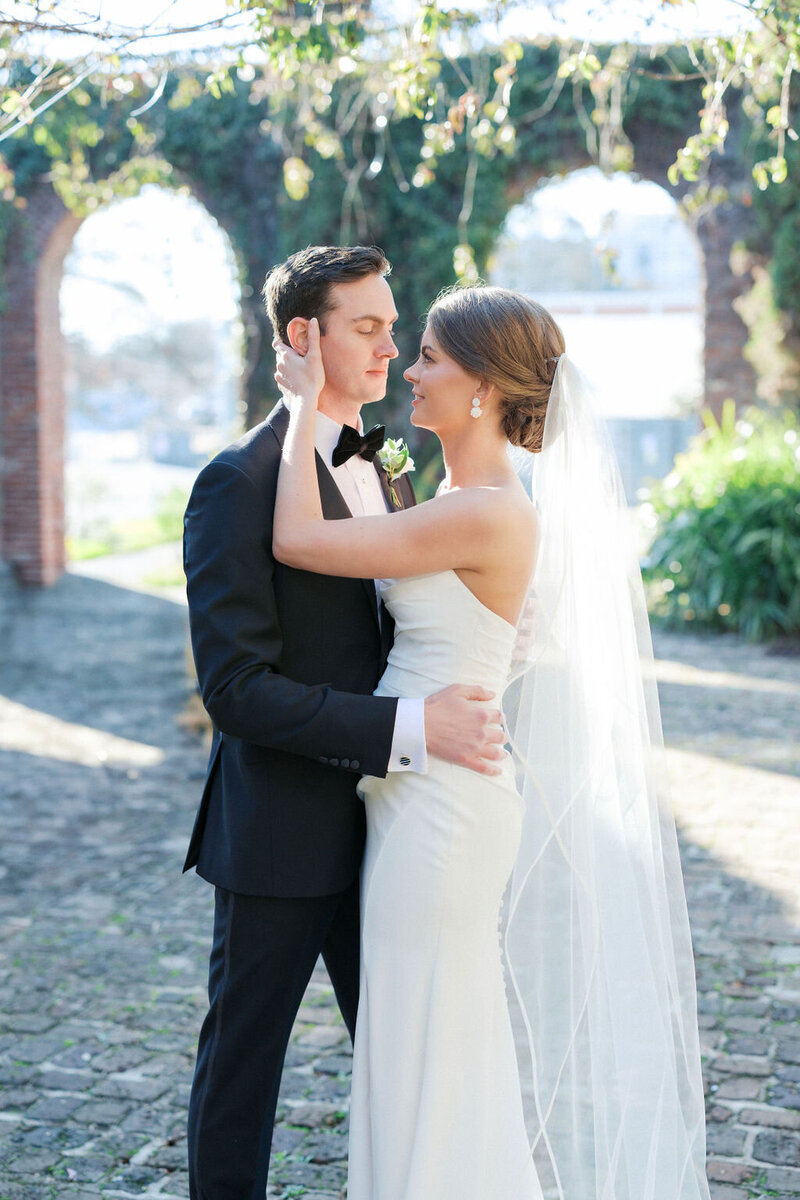 Bride in white dress holds grooms face underneath arches overgrown with ivy at at Summerour Studio