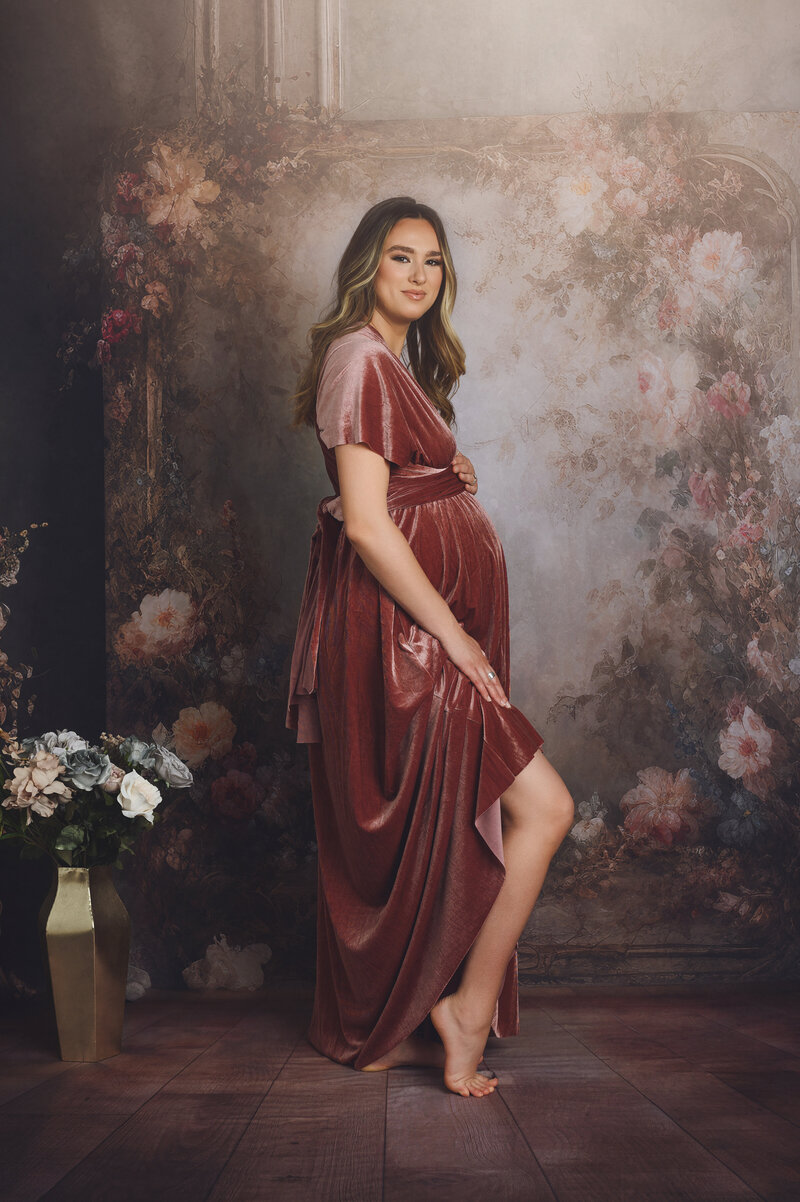 Pregnant woman in a burgundy dress posing by a floral background