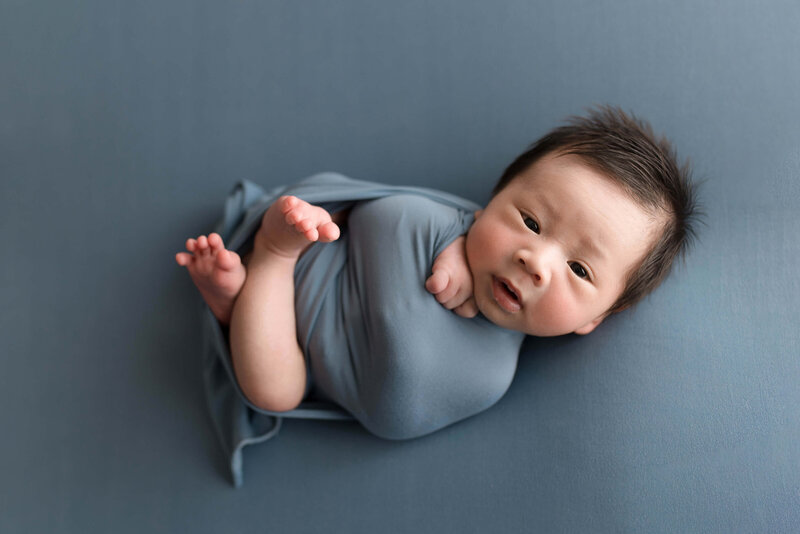 Cute baby boy wrapped in blue fabric on blue backdrop