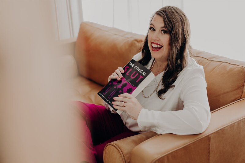 woman smiling while holding 'the ethical slut' book against her chest