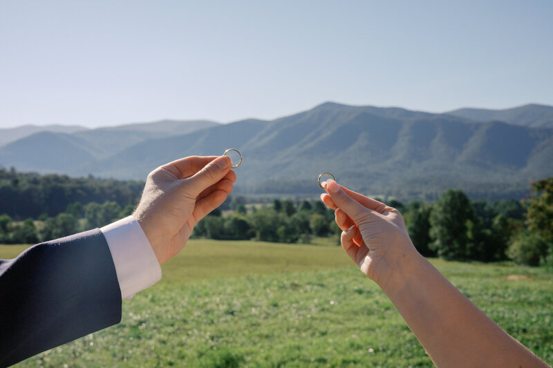 A bride and groom holding their wedding rings with a mountain in the background in Tennessee.