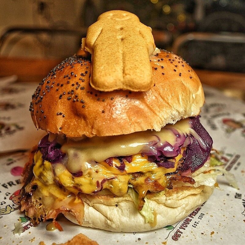 A street food patty burger in a brioche bun with cheese and sauce dripping out with a gingerbread man on top