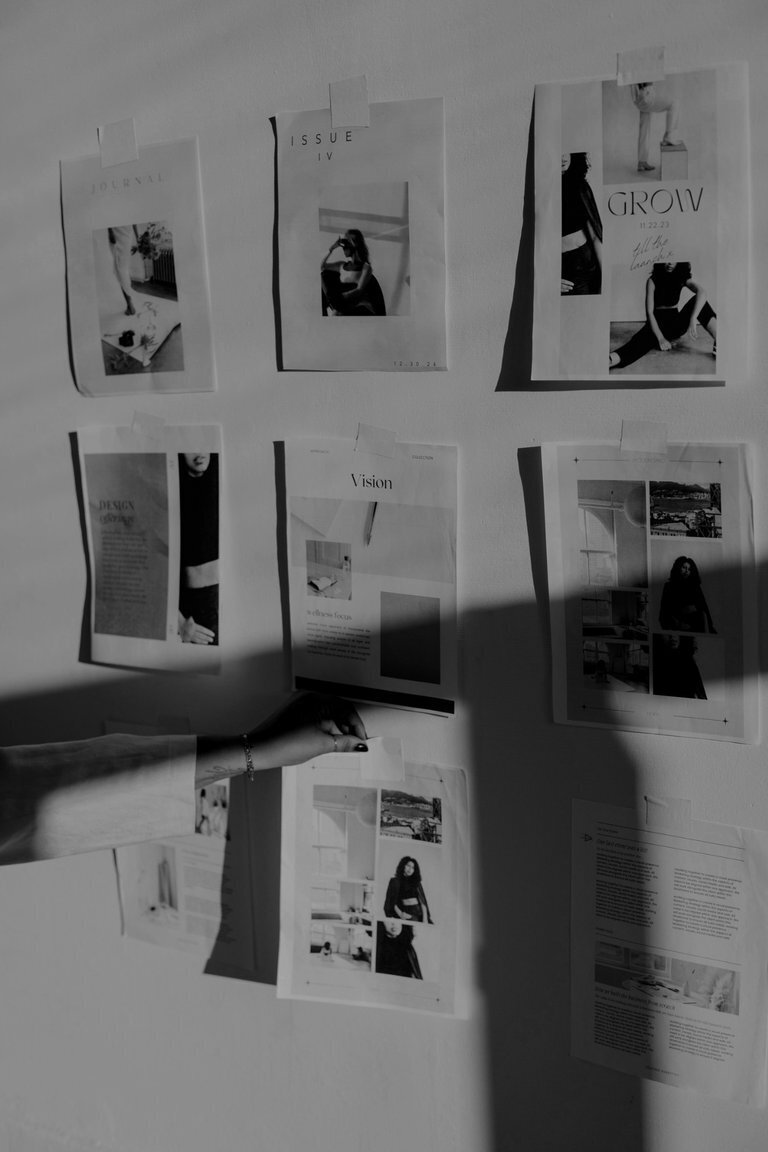 Moodboard of editorial-style design prints on a wall, with a hand adjusting one, symbolising visual strategy, storytelling, and brand alignment.