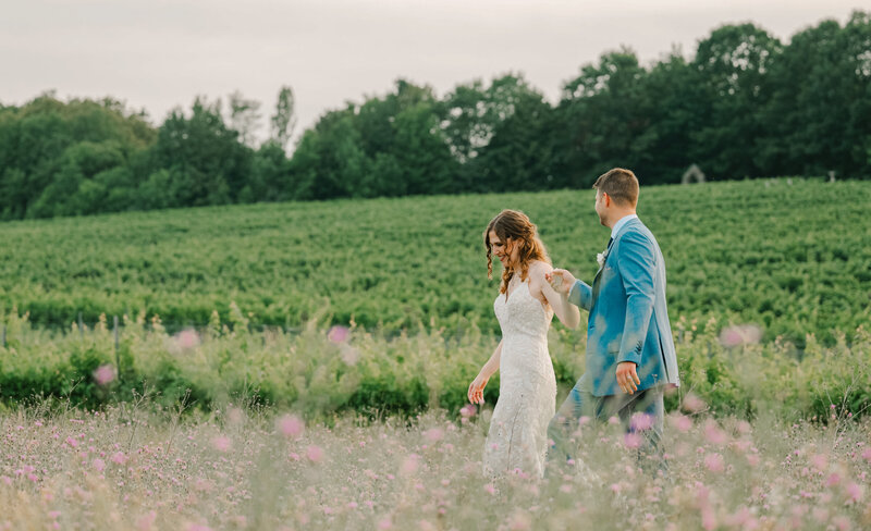 A bride and groom walks in a field  with their Michigan wedding photographer