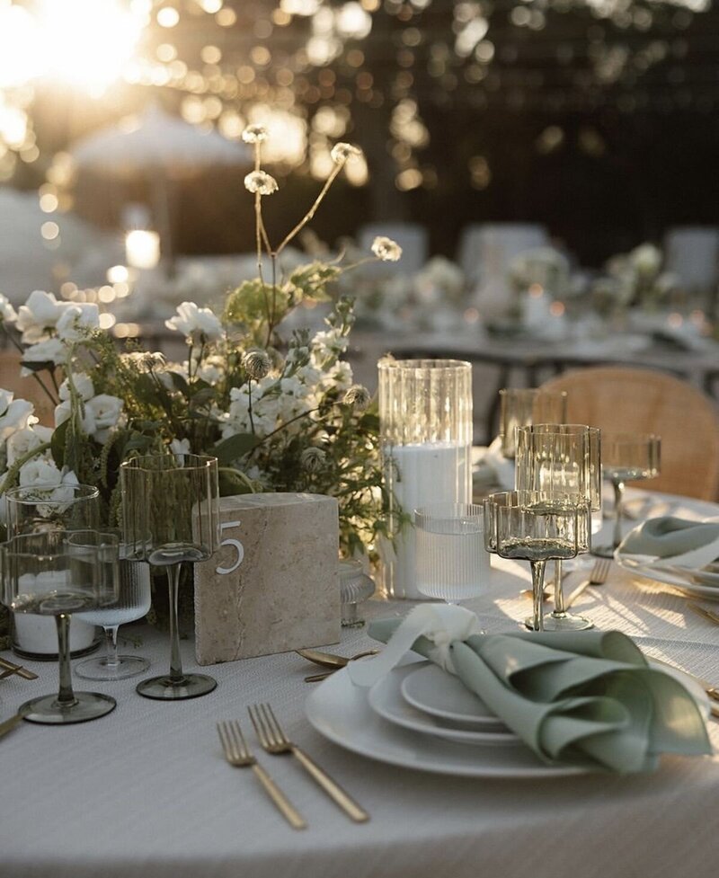 Garden wedding at sunset featuring green and ivory florals and matching place settings.