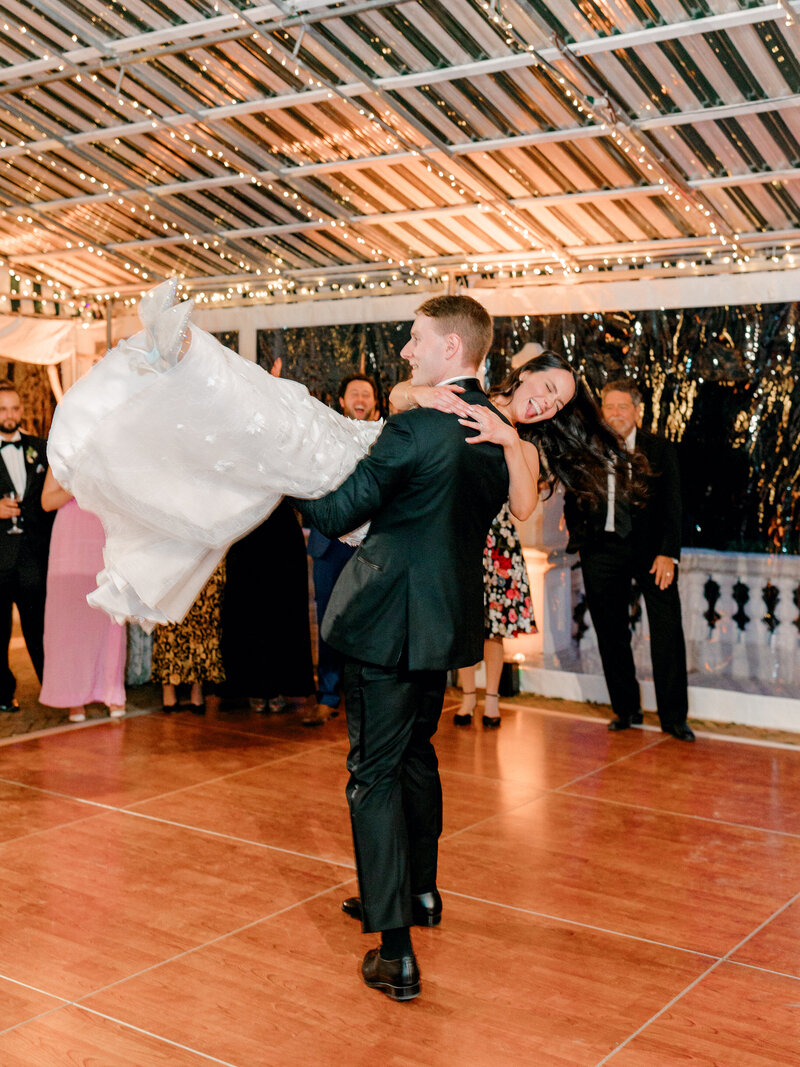 Groom lifts and spins bride with guests watching in the background