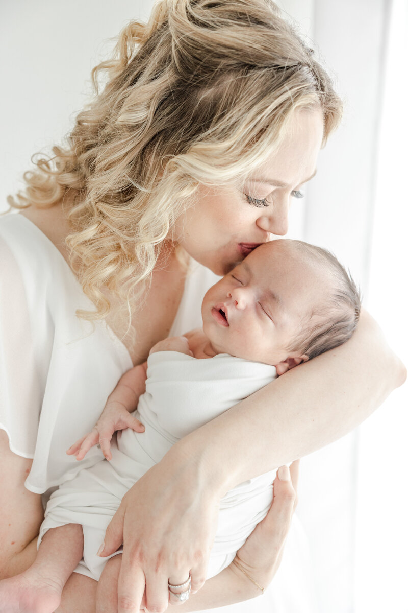 New mom kisses her newborn baby boy's forehead during newborn portrait session