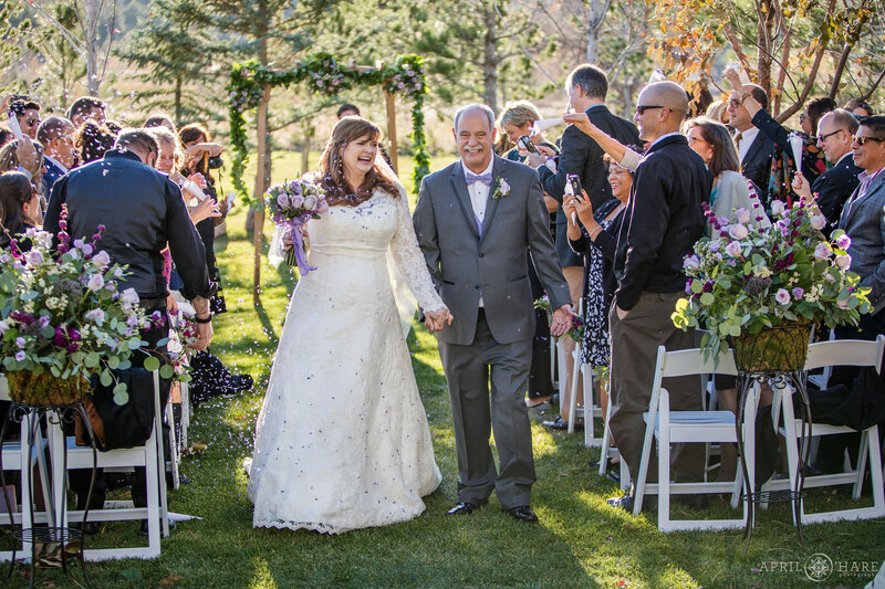 Couple walks hand in hand down the aisle together at the end of their outdoor wedding ceremony on the Cabin Lawn in Boulder CO