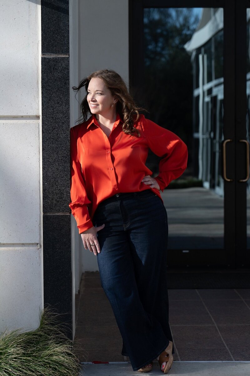 woman in red shirt leaning against a building and looking to the right