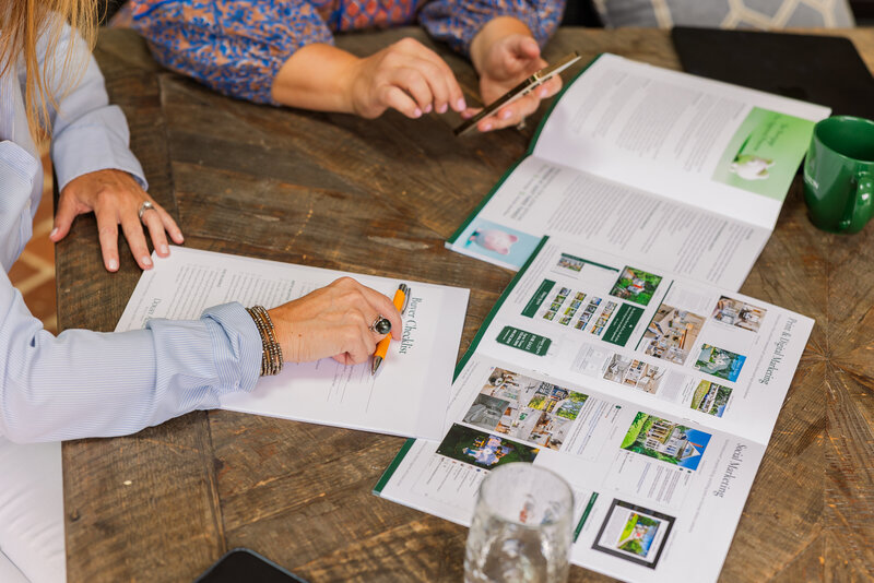 details of women working on a wooden table with paper, pen and brochure during branding photoshoot with Laure Photography Atlanta