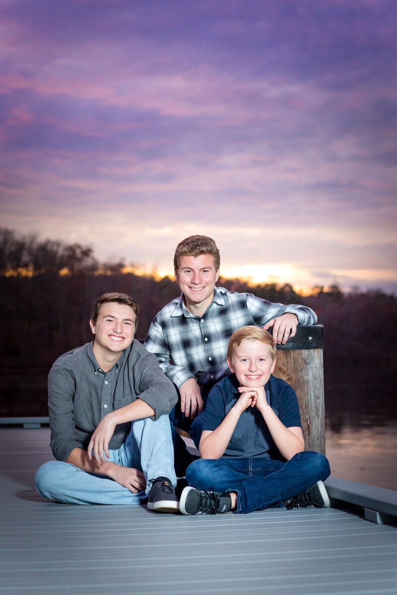 Three sons sitting on a dock over  Lake Peachtree. with a purple sunset.