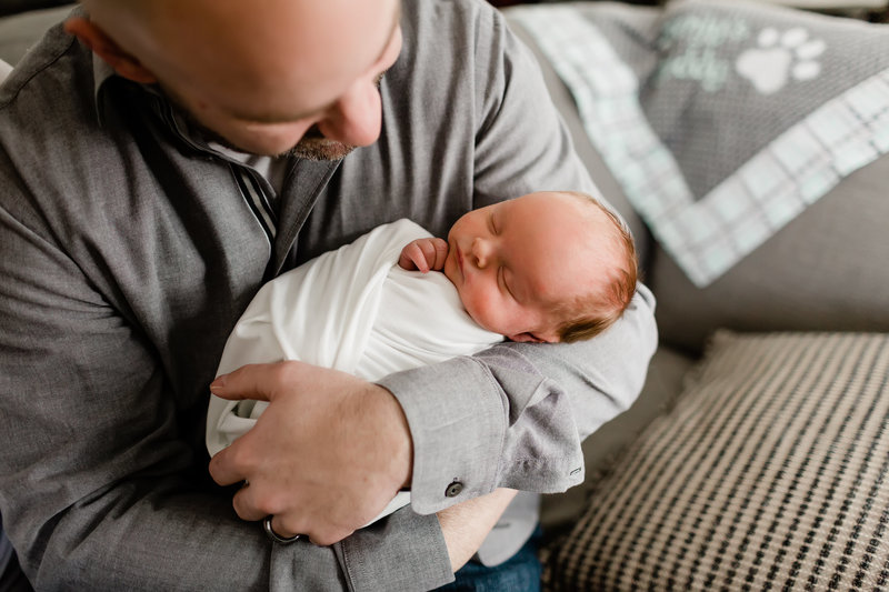 Dad holding swaddled newborn baby girl on couch