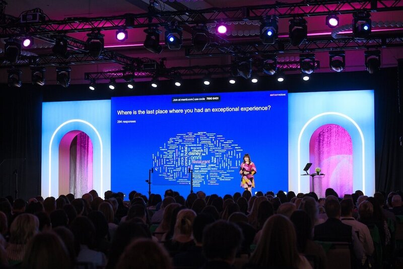 Brittany Hodak using Mentimeter on stage with a word cloud beind her.