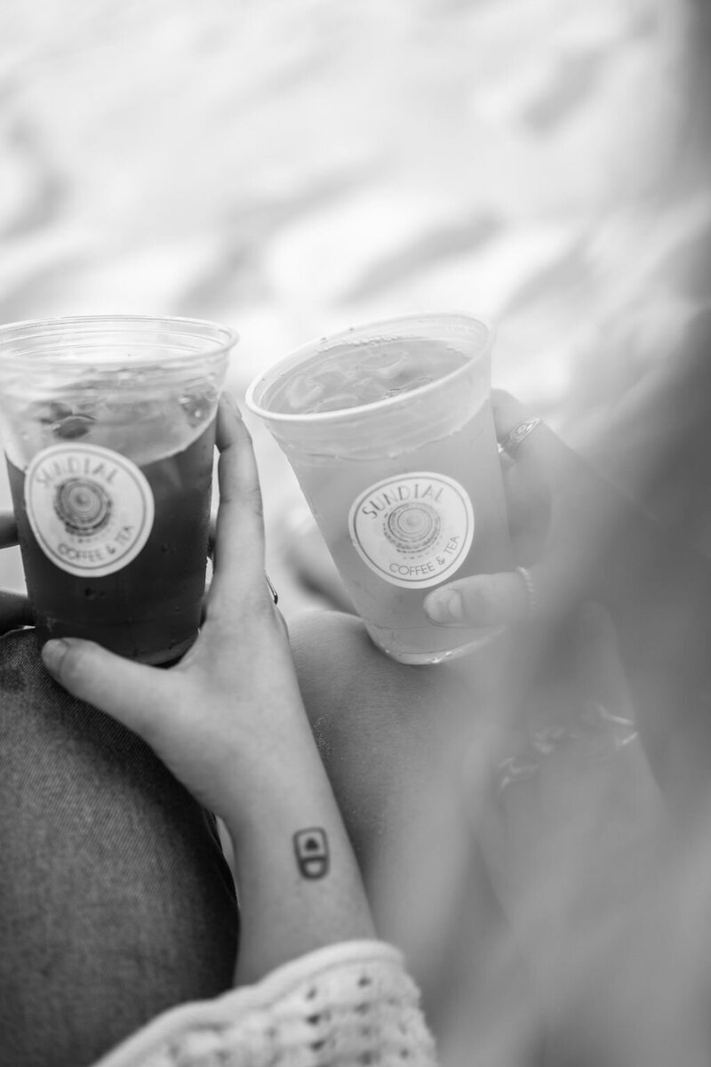 a black and white photograph of two people holding their sundial iced teas