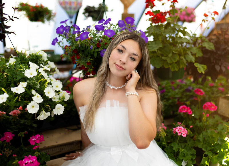 Senior girl photo session in agreenhouse with white dress surrounded by flowers.