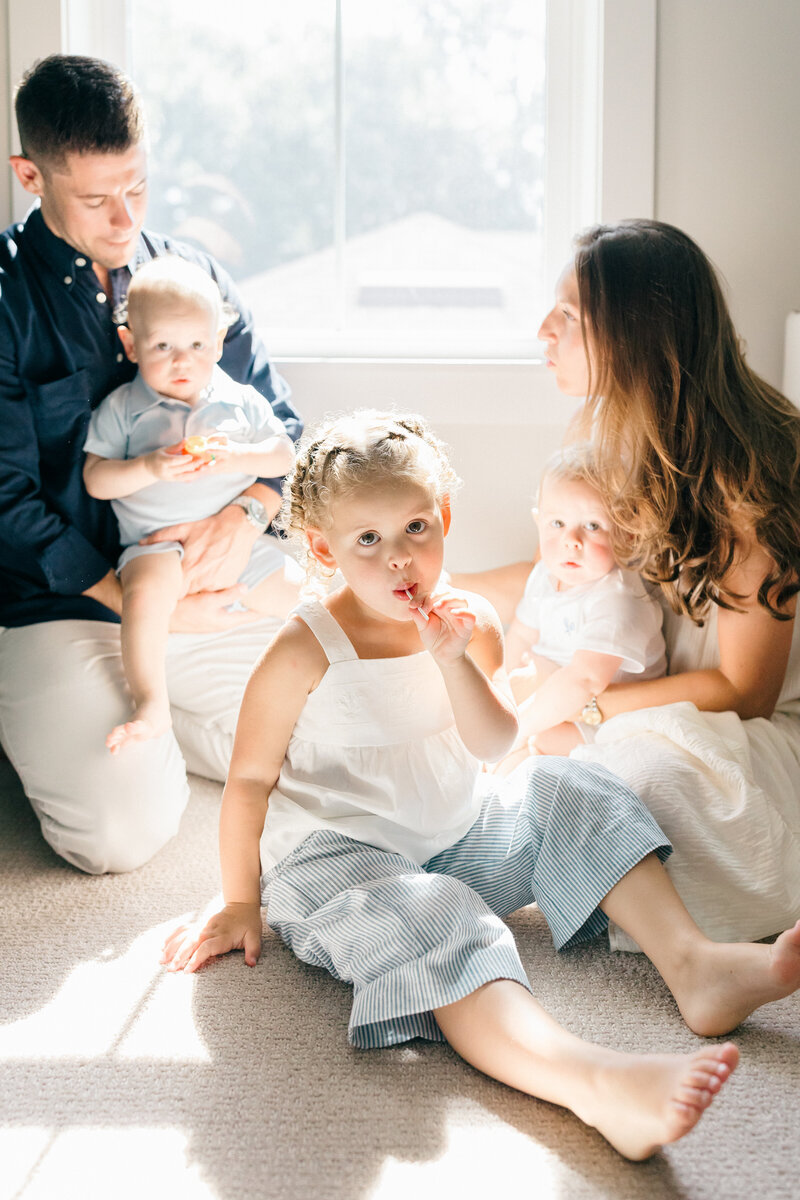 Toddler sits on floor enjoying lollipop with the Tampa sunshine beaming through the windows during at home family photo serssion