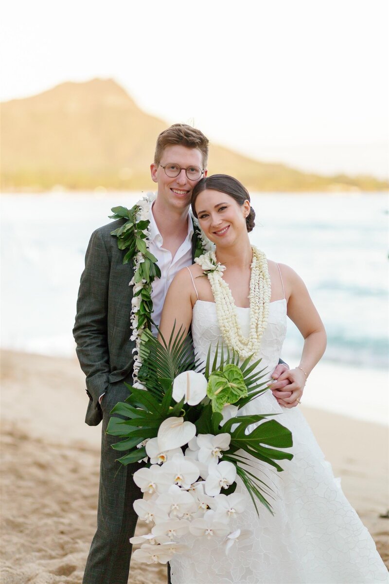 A wedding couple standing on a beach with their arms around each other 