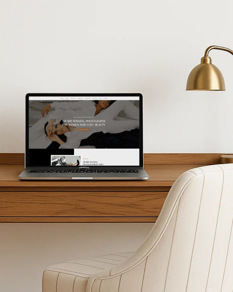 A beige chair sits at a small, wall-mounted desk. On the desk is a gold lamp and a macbook pro laptop displaying a website built by Cornerstone Digital Studio.