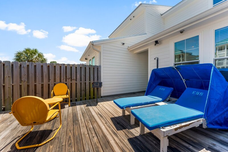 Private outdoor deck with vintage yellow chairs, charcoal grill, and covered loungers at Groovy Shack in Panama City Beach near Alys Beach.