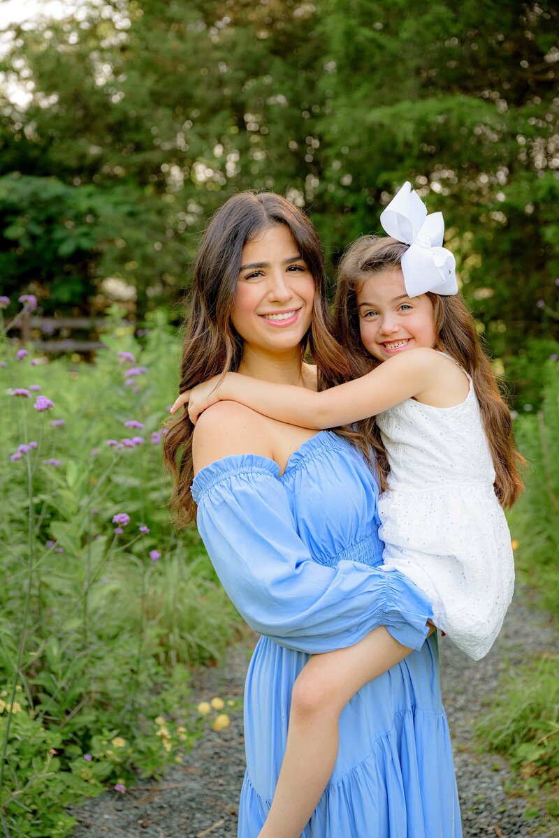 mother dressed in blue holds her daughter on her hip
