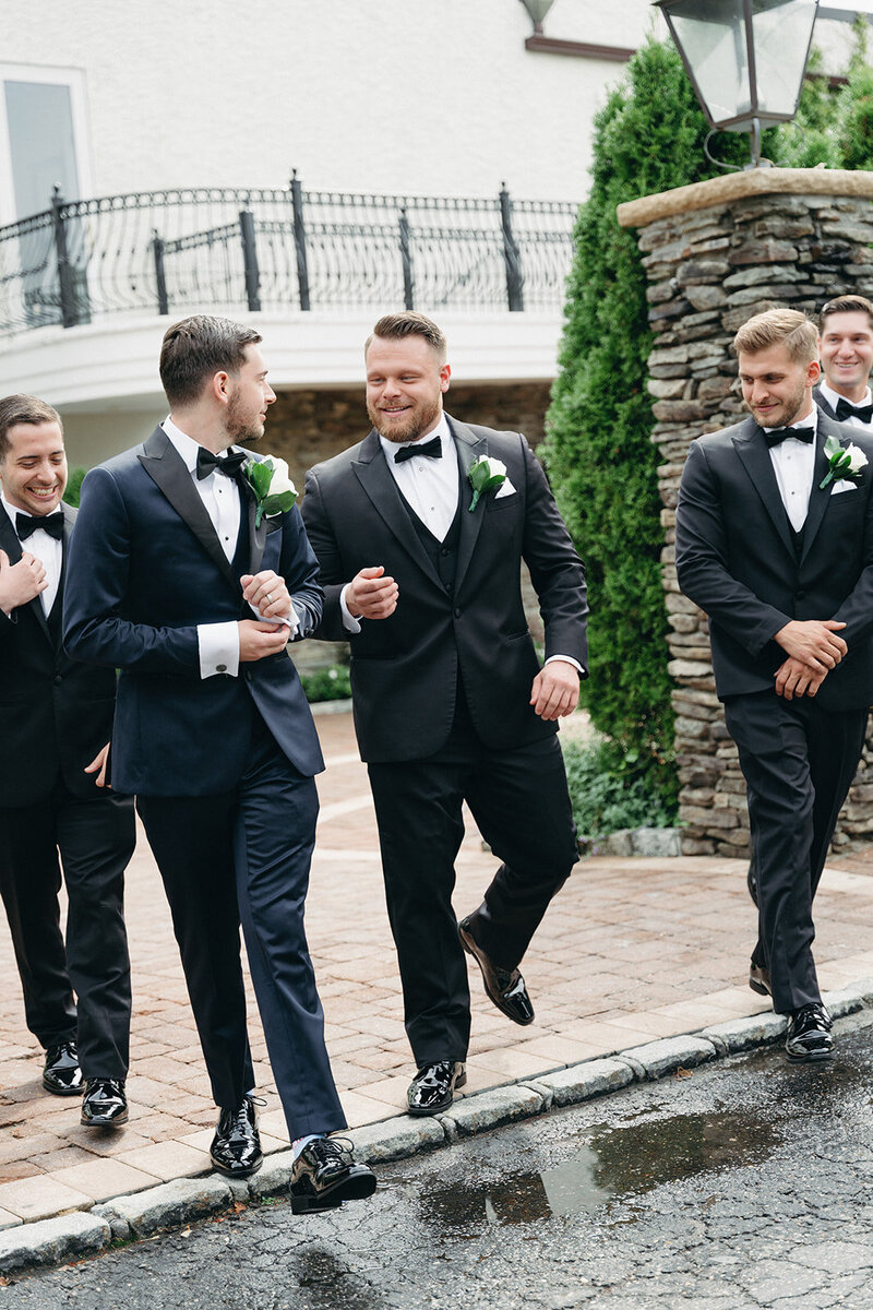 Groomsmen walk and talk together dressed in their black tuxes. 