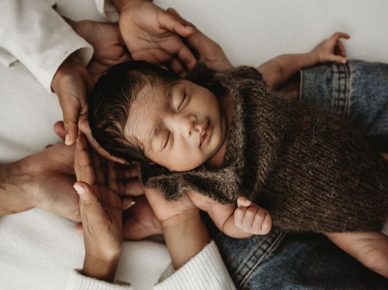 Serene studio portrait of a newborn baby sleeping soundly on a plain light beige surface, adorned with a beautiful gold crown and wearing a soft white romper