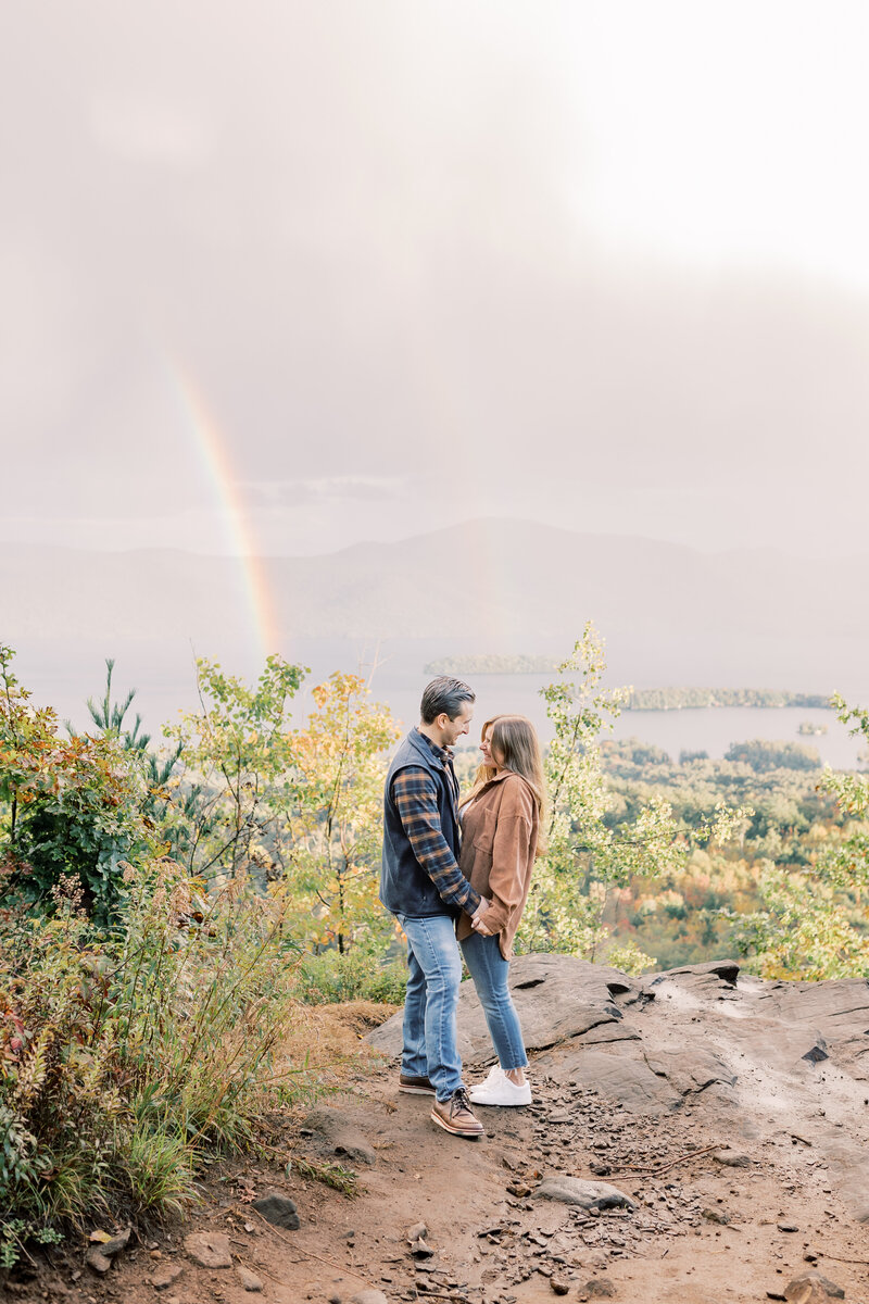 On top of a mountain in  Lake Placid a couple posed for their engagement photos. With the Adirondack mountains in the background a rainbow appeared in the sky as we reached the peak.