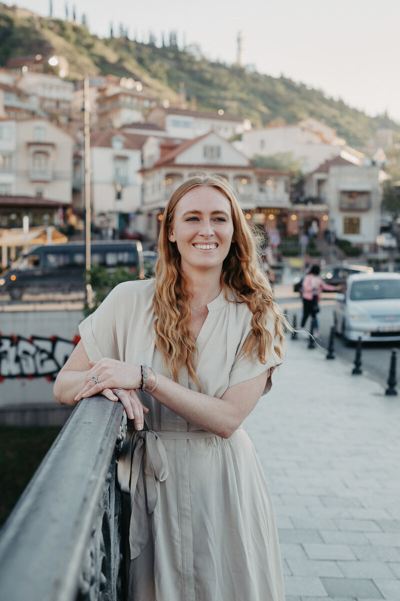 Kara stands smiling on a bridge in European city