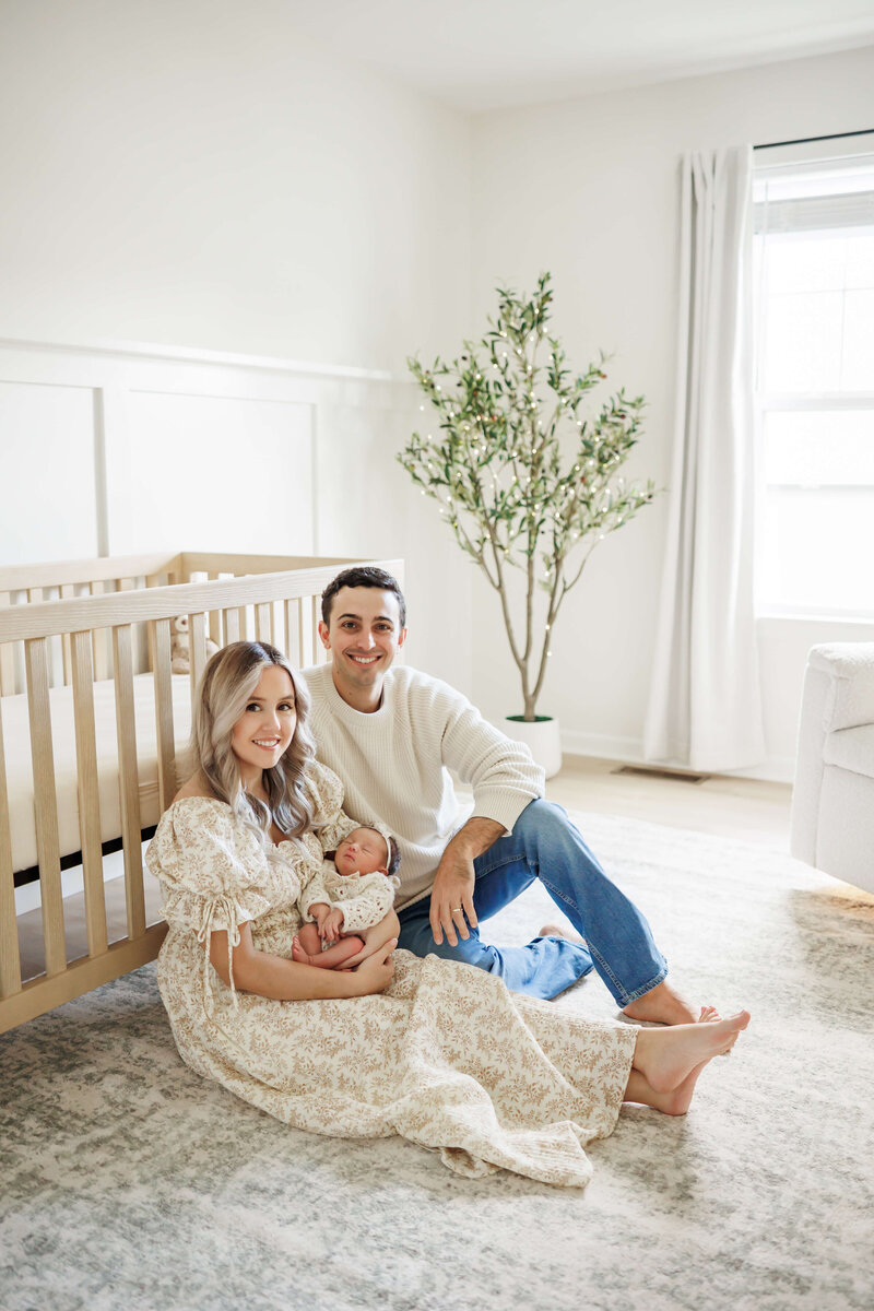 mom, dad, and newborn baby girl sitting on the floor of a neutral nursery in harrisburg pa lifestyle newborn session