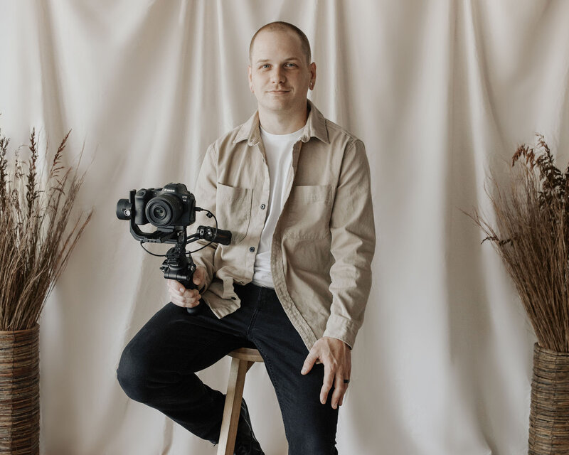 Joshua McElroy sitting on stool and holding camera on a tripod