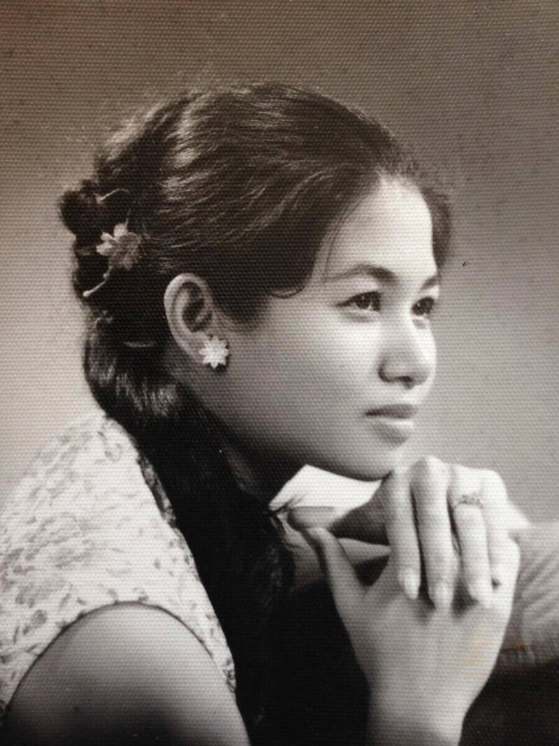 Sepia engagement portrait of a young Nita Tin wearing a floral dress with manicured nails and a flower in her hair, gazing lovingly toward her future husband, Pe.