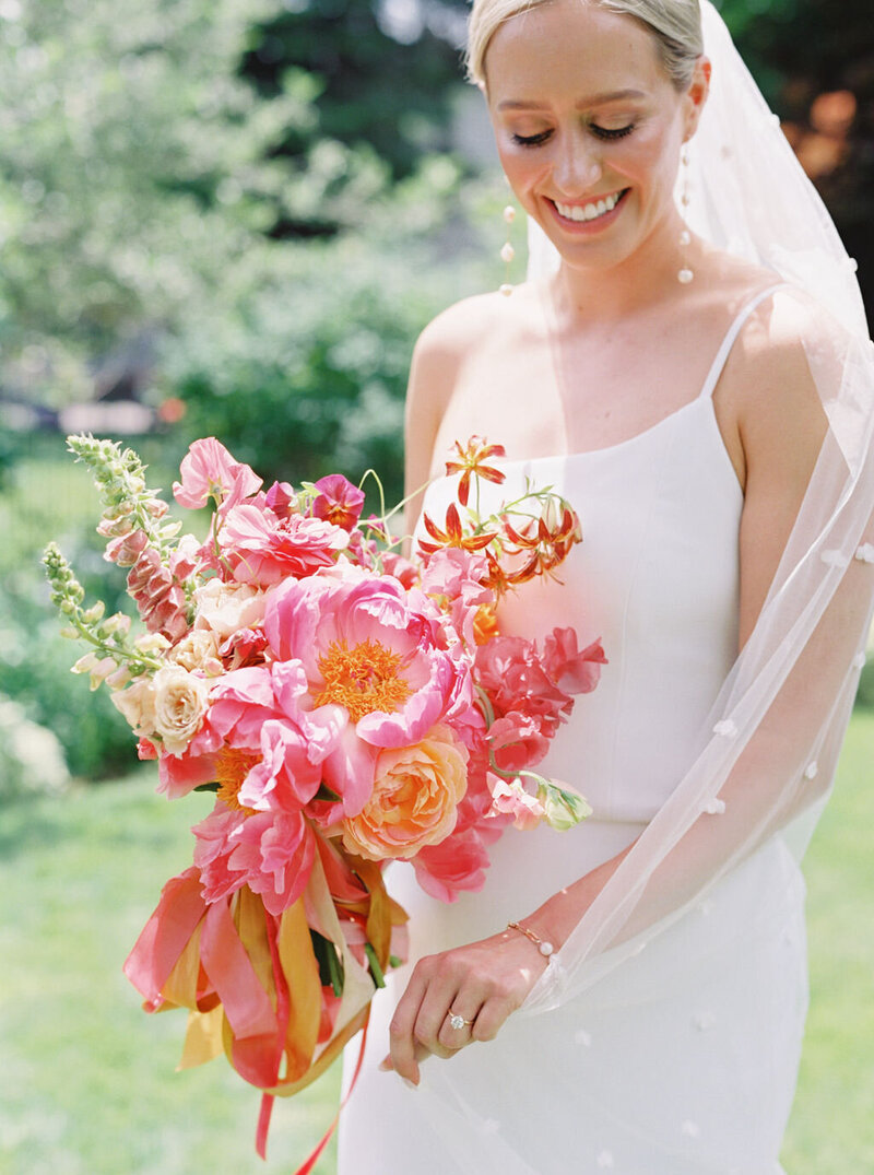 Bride Kelly holding her vibrant summer bouquet with coral, peach, and blush peonies, ranunculus, foxglove and lilies, styled with seasonal textures by Summer Robbins Flowers in Bend, Oregon