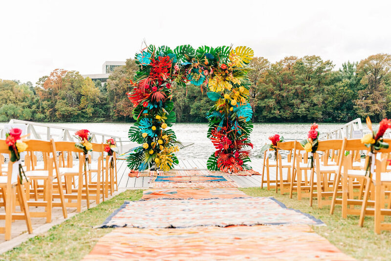 Bold and colorful tropical floral wedding arch on a waterfront dock, part of a creative outdoor wedding planned in Austin, Texas.