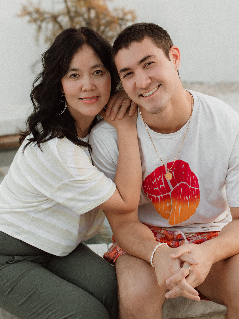 Portrait of photographer Jess Young sitting closely with her son, both smiling at the camera in their Canyon Lake backyard — a personal glimpse into the heart behind her family and newborn photography.