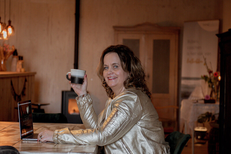 Jacqueline geniet van een kop koffie tijdens een coaching sessie, met een laptop open voor haar.