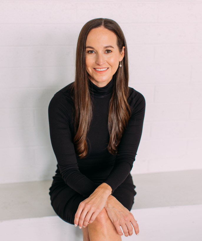 Dr. Kristie Overstreet  wearing a black dress, sitting on a bench, smiling at the camera.