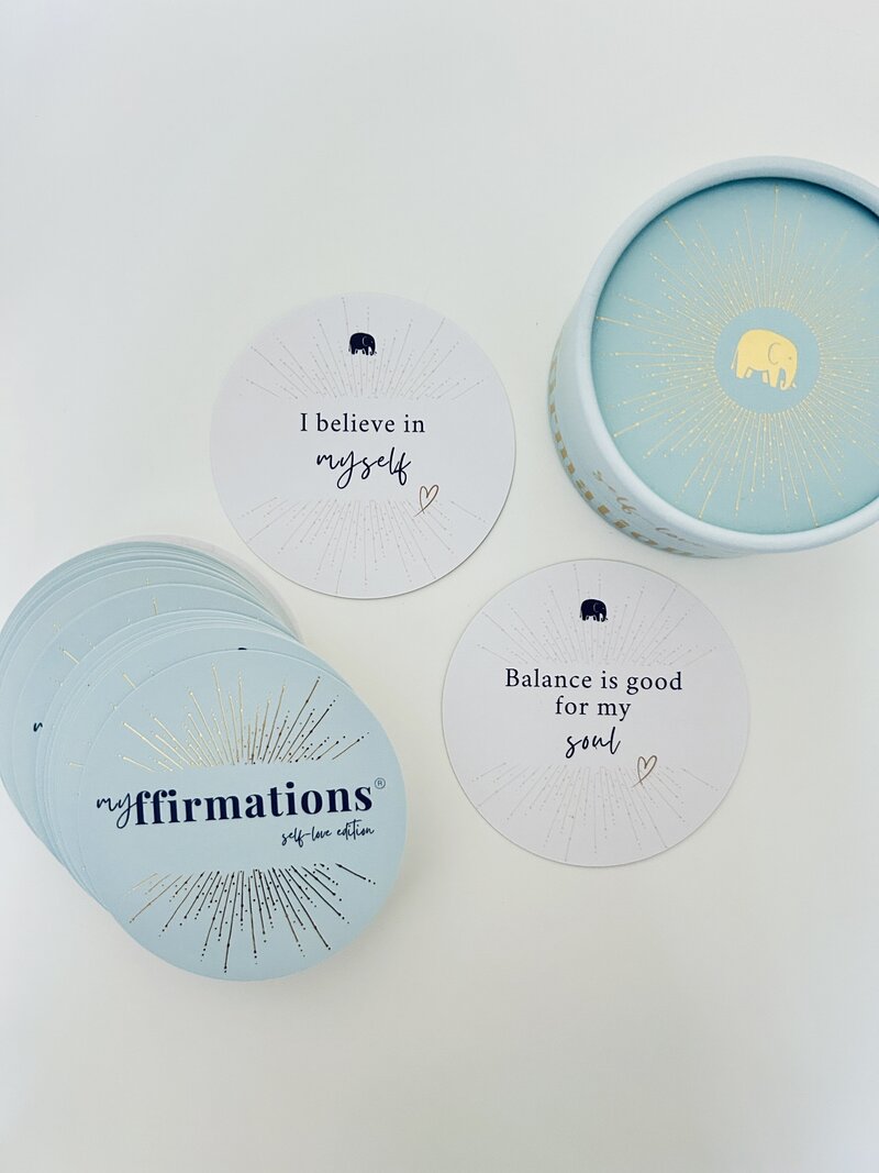 Image shows myffirmations positive affirmation cards on a white background. One card reads 'I believe in myself' and the other card reads 'Balance is good for my soul'. There is a slightly fanned stack of cards on the bottom left with the myffirmations logo visible. The card box is shown in the top right corner