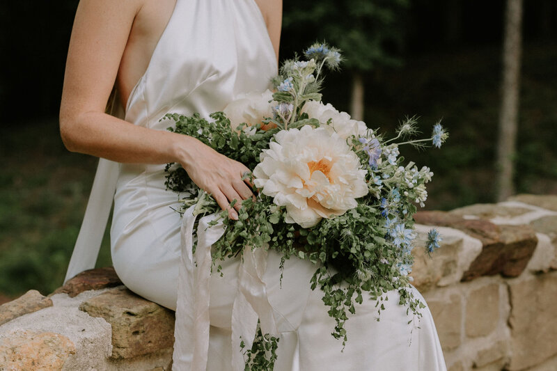 A Nashville bride sitting on a stone wall holding a large bouquet