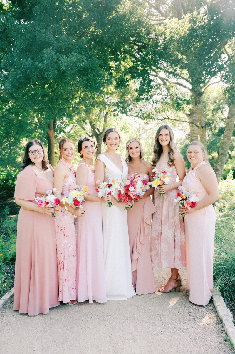 bride and bridesmaids in mixed pink dresses with bright spring floral bouquets by caroline james florals at ladybird johnson wildflower center by austin wedding photographer