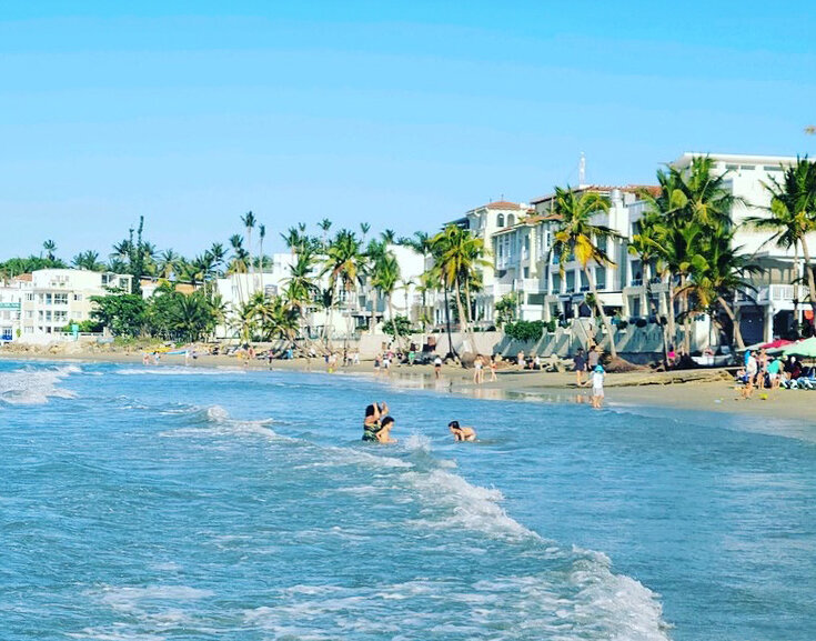 Parents and children playing in the ocean near a Dominican resort community