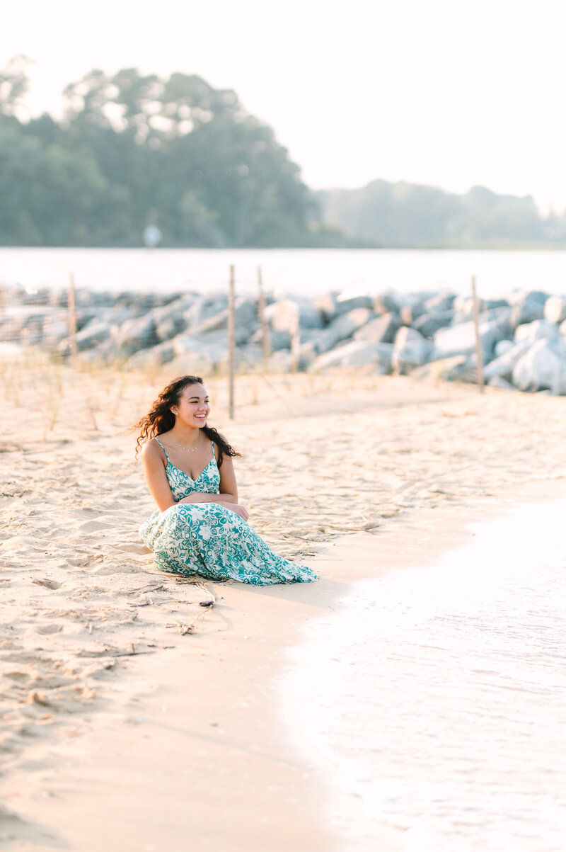 a young woman smiling while sitting on the beach in a green dress