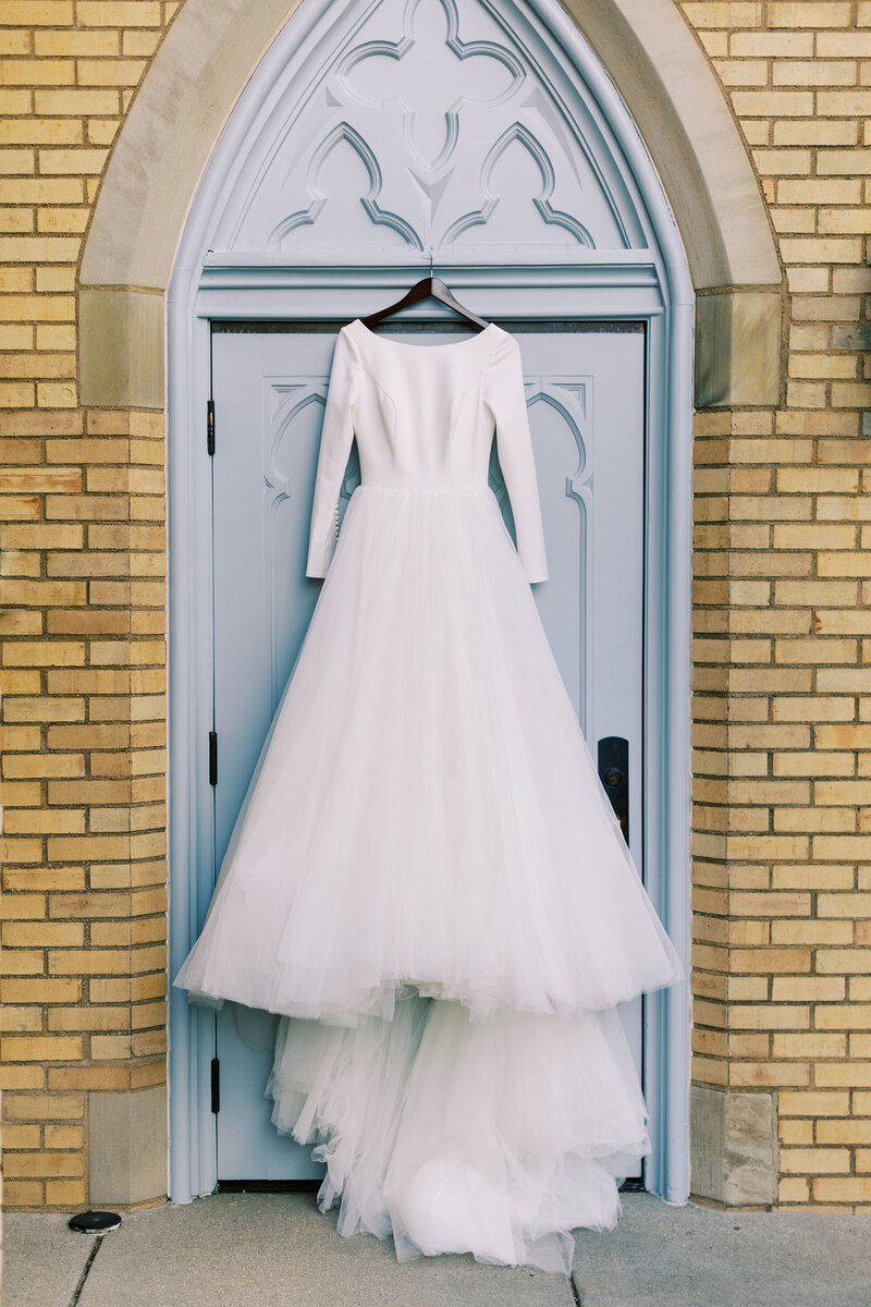 Bridget's wedding dress hangs on blue door of Cathedral of Saint Andrew's for their Grand Rapids Wedding, photo by Cynthia Mae Photography